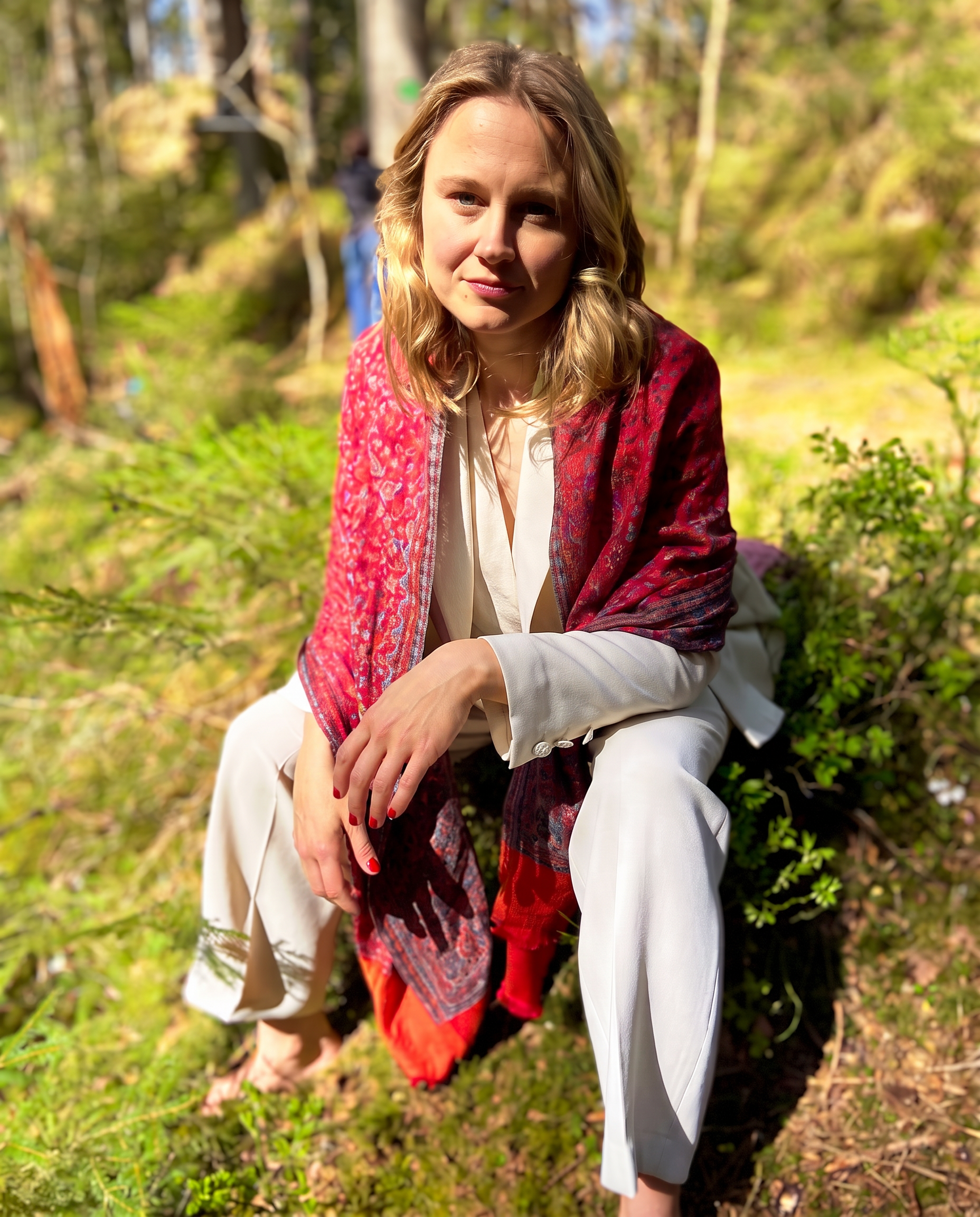 Anna Ma seated in a sunlit forest wearing a red scarf